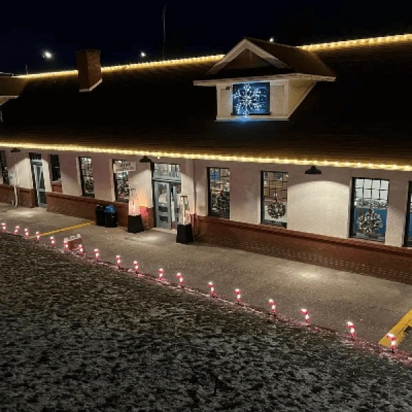 Building facade at night with string lights and festive decorations, snow on the ground.