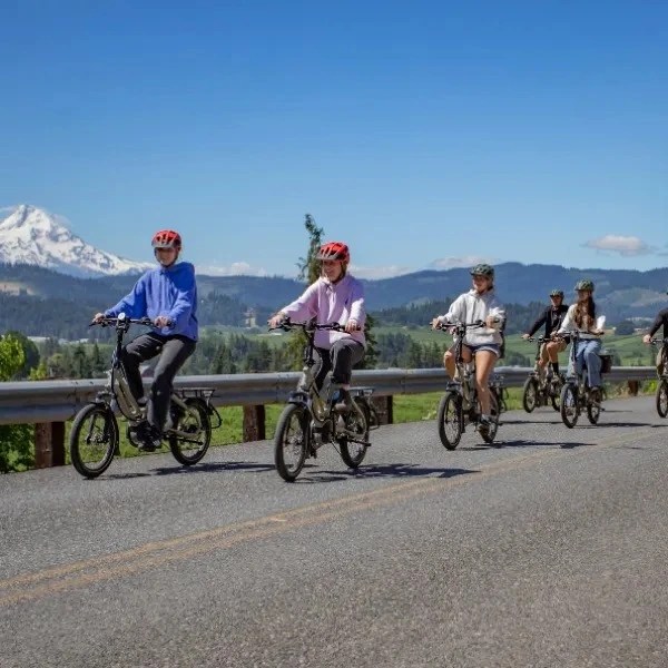 Group of people cycling on a road with a mountain and blue sky in the background.