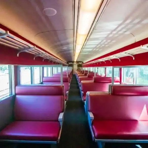 Interior of an empty train car with red seats and overhead luggage racks.