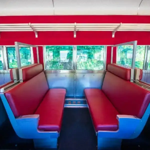 Retro train interior with red seats and wood trim, facing each other in a small compartment.