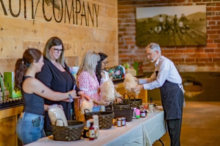 Four people receiving products from a man at a table in a wooden and brick room.